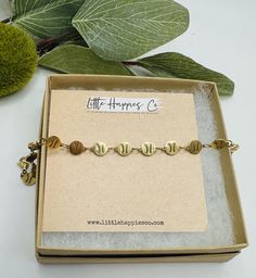 the little hope bracelet is in its box and sits next to some green leaves on a white table