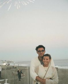 a man and woman standing next to each other in front of the ocean with fireworks