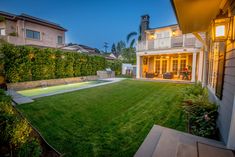 the back yard is lit up at night with lights shining on the lawn and pool in the distance