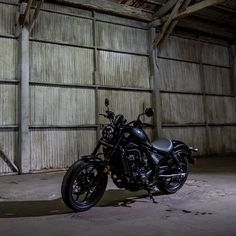 a black motorcycle parked in front of a garage with no doors on the side and an open door behind it