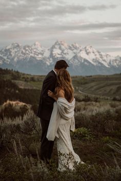 a bride and groom embracing in front of the mountains