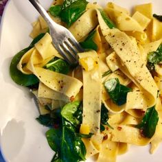 a white plate topped with pasta and spinach covered in seasoning next to a fork