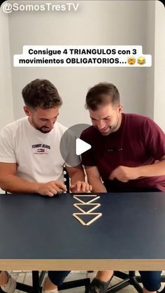 two men are sitting at a table and one is playing with some sort of object