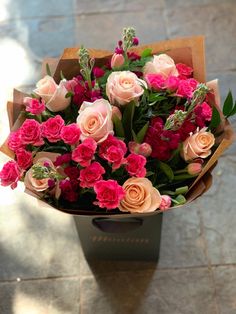 a bouquet of pink and orange roses in a brown paper wrapper on the ground