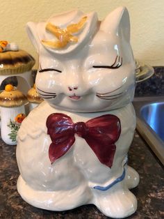 a white ceramic cat with a red bow on it's head sitting on a counter