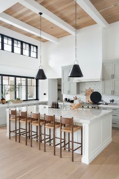 a large kitchen with white cabinets and wooden flooring, along with an island that has four bar stools