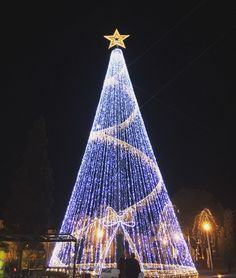 a large christmas tree is lit up with blue and white lights in the shape of a star