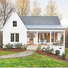 a small white house with a porch and covered front door in the country side yard