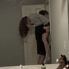 a woman standing on top of a bathroom counter next to a teddy bear and blow dryer