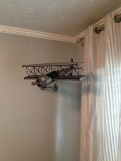 an airplane hanging from the ceiling in a room with white walls and striped drapes