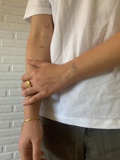 a person with a small tattoo on their arm holding onto another persons hand, both wearing gold rings