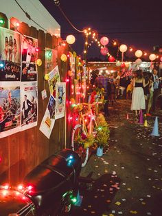 an outdoor event with lights and posters on the wall, people walking down the street