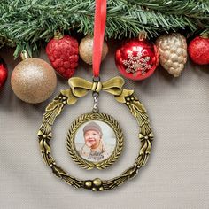 a christmas ornament hanging from a tree with ornaments around it and a red ribbon