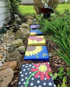 painted stepping stones are lined up on the ground in front of some plants and rocks