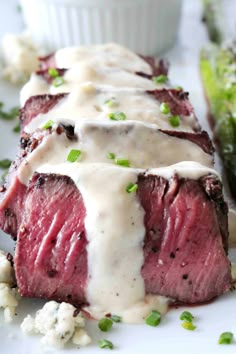 the steak is covered in white sauce and garnished with green onions