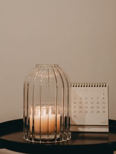 a candle sitting on top of a table next to a calendar and a birdcage