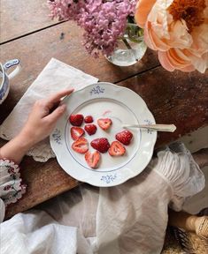 a plate with strawberries on it sitting on a wooden table next to some flowers