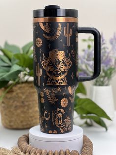 a black and gold travel mug sitting on top of a white table next to some plants