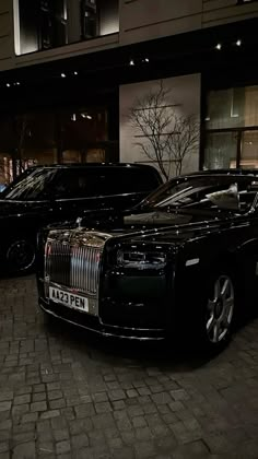 two rolls royces are parked in front of a building on a brick street at night