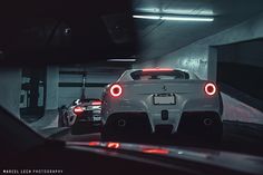 two white sports cars parked in a parking garage with red lights on the taillights