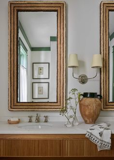 a bathroom with two mirrors and a vase on the counter next to eachother