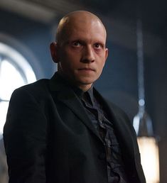 a bald man in a black suit and tie looking at the camera with an evil look on his face