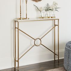 a console table with vases and flowers on it in front of a white wall