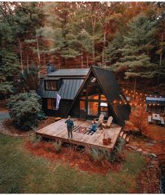 two people standing on a deck in front of a cabin with lights strung from the roof