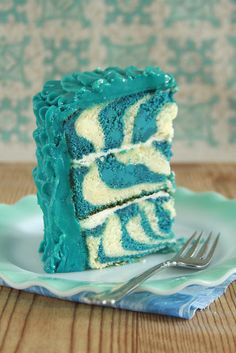 a piece of blue and white cake on a plate with a fork next to it