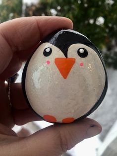 a hand holding a rock with a penguin painted on it