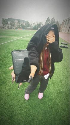 a woman in black hoodie holding up a suitcase on grass with other items around her