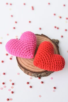 two crocheted hearts sitting on top of a piece of wood