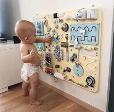 a baby standing in front of a wall with magnets on it's side