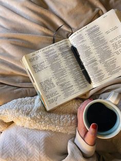 a person laying in bed with an open book and cup of coffee