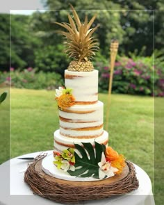 a three tiered cake with pineapple and flowers on top sits on a table outdoors