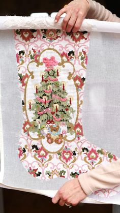 a woman holding up a christmas stocking with a cross - stitch tree on it