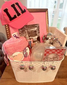 a pink hat and other items in a white basket on a wooden table next to a framed photograph