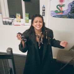 a woman with long hair standing in front of a white wall and smiling at the camera