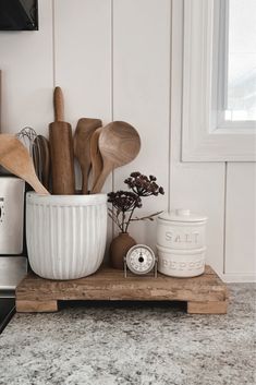 kitchen utensils and wooden spoons in a white bowl on a wood tray