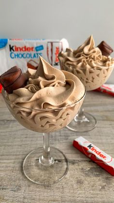 two glasses filled with ice cream on top of a wooden table next to candy bars