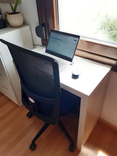 a laptop computer sitting on top of a white desk next to a window in an office