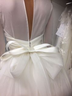 the back of a white dress with a bow on it's belt, in front of a mannequin