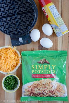 ingredients to make an egg and cheese sandwich laid out on a wooden table with waffle iron