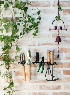 garden tools hanging from hooks on a brick wall