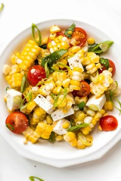 a white bowl filled with corn salad and topped with feta cheese, tomatoes, green leaves