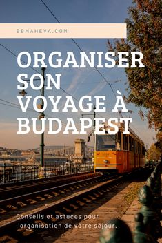 an orange train traveling down tracks next to a tree and water with the words organier son voyage a budapest