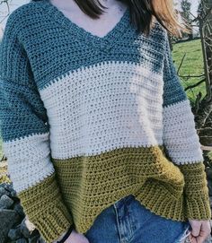 a woman standing in front of a rock wall wearing a green and white crochet sweater