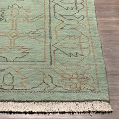 a green rug with an intricate design and fringes on the bottom, sitting on a wooden floor