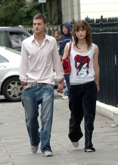 a man and woman walking down the street holding hands with one another, both looking at something