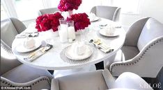 the table is set with white chairs and red flowers in vases on each side